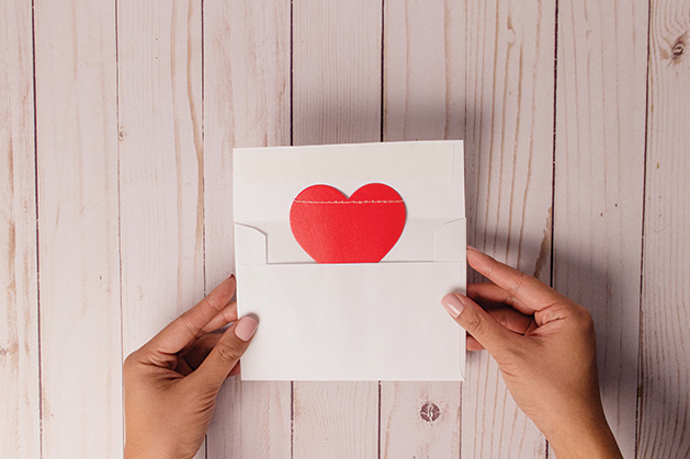 A red heart coming out of a white envelope
