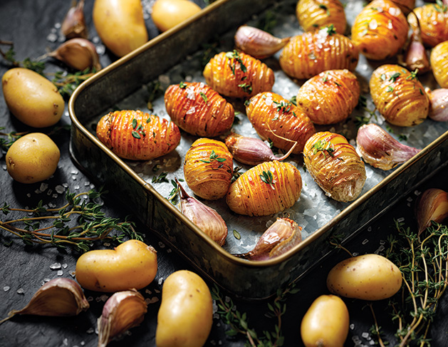 Baked potatoes hasselback with garlic and thyme in a baking dish close up view