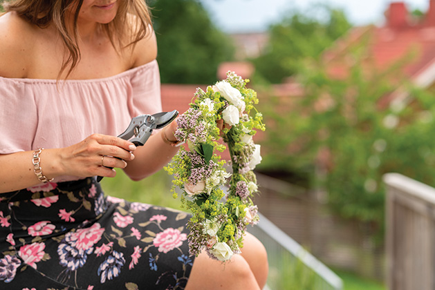 A woman in Sweden is making floral crown for midsummer celebrations on a summer day. Traditional Swedish wreath.