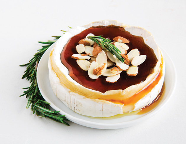 A wheel of brie cheese covered in honey and almonds.