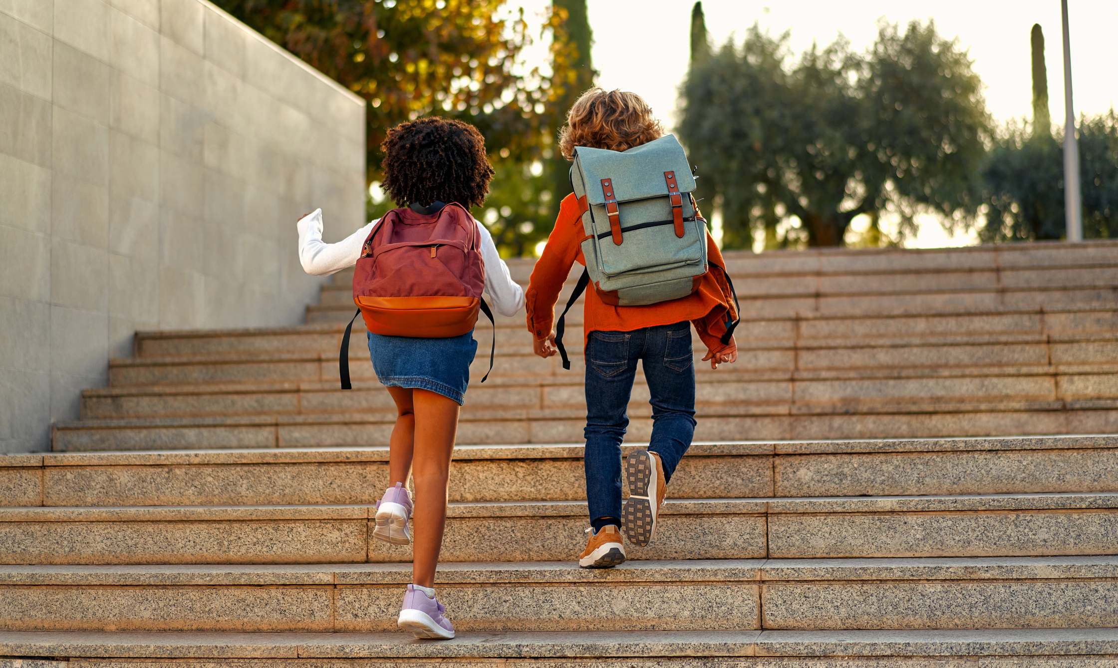 Happy smart kids with school bags rush to the lessons to school running up the stairs. Back to school. An African-American schoolgirl and her classmate walk down the street after school.